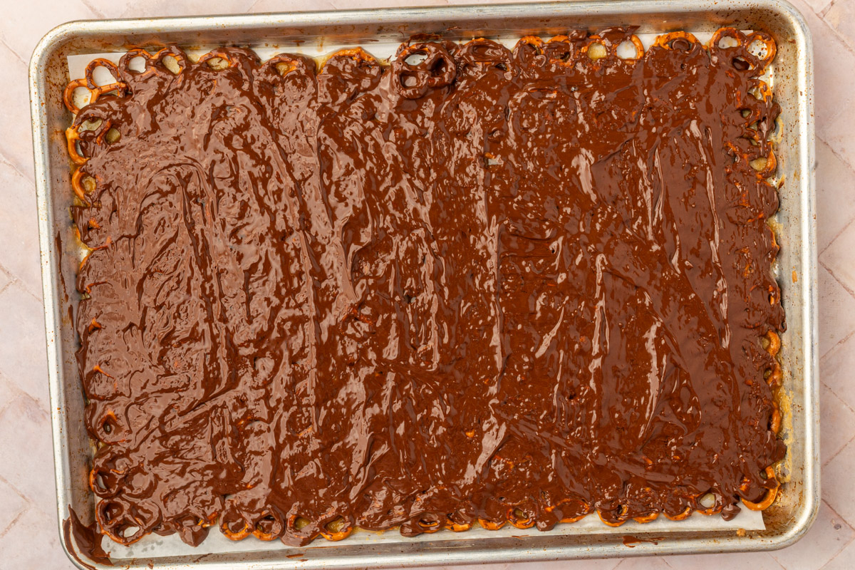Smooth melted chocolate spread over caramel pretzel bark with spatula.