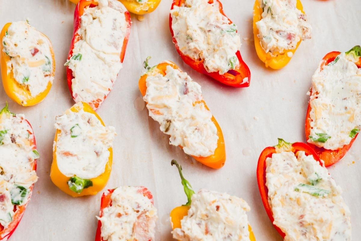 Mini sweet peppers stuffed with cream cheese on a parchment-lined baking sheet before baking.