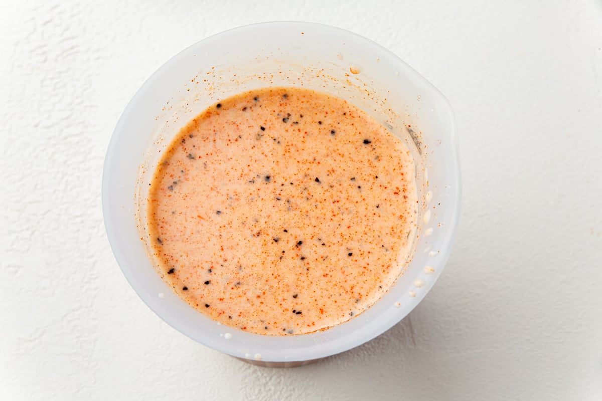 Buttermilk marinade for gluten-free fried chicken in a white bowl with pickle juice and spices.