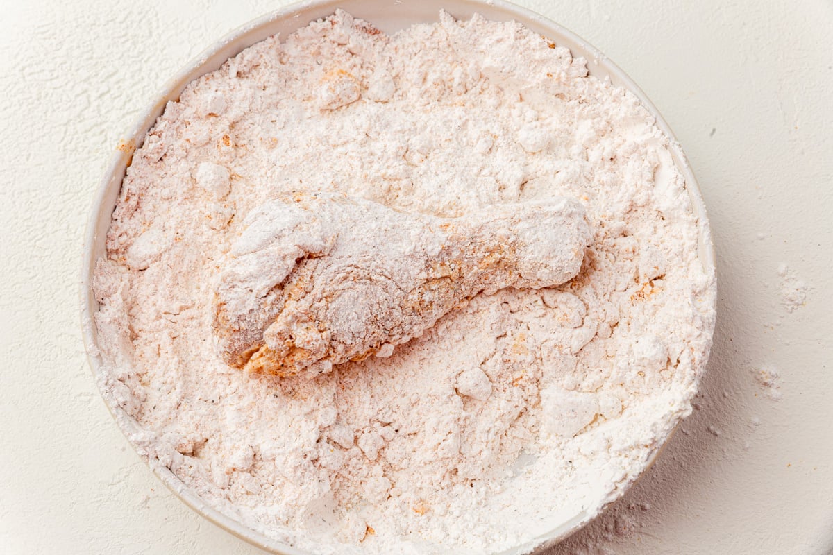 Chicken piece fully coated in gluten-free flour mixture ready to fry.