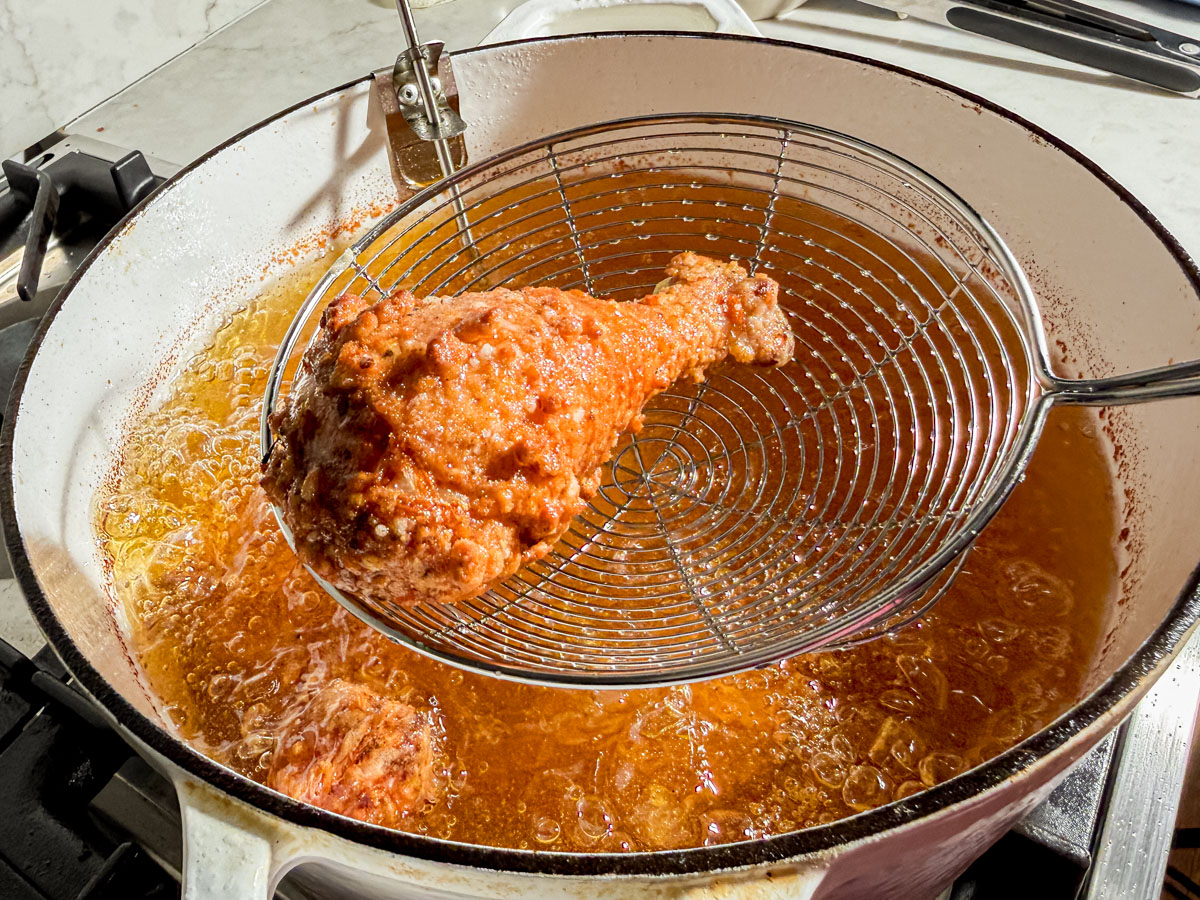 Gluten-free fried chicken piece being removed from frying oil with a spider spatula.