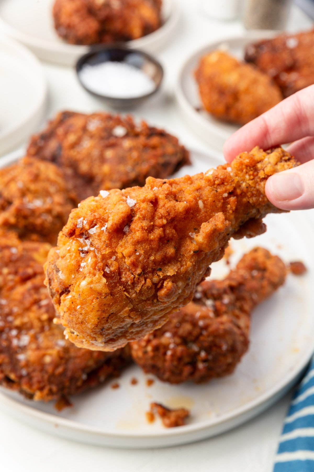 Hand holding crispy gluten-free fried chicken drumstick showing light crunchy coating.