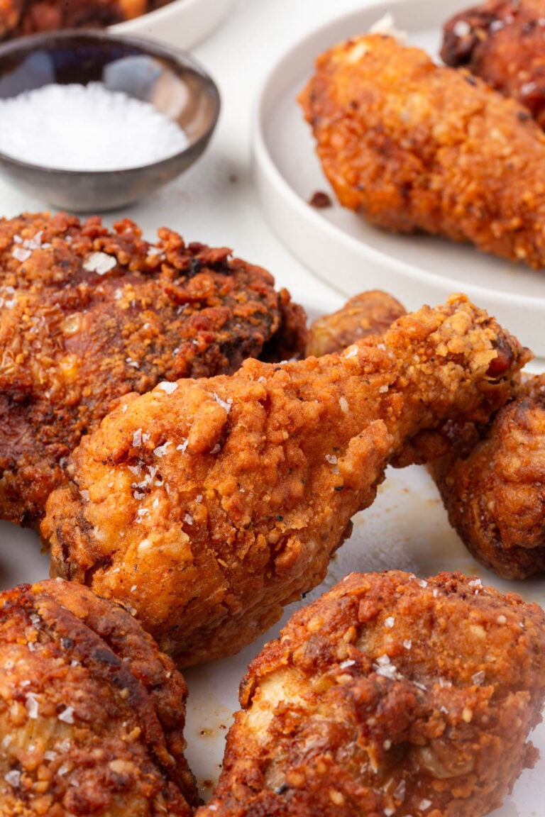 Gluten-free fried chicken thighs and drumsticks on white platter with flaky salt.