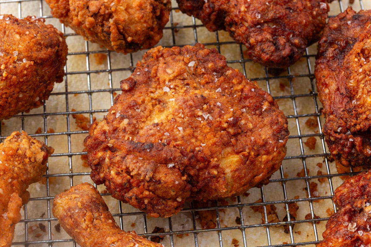 Crispy gluten-free fried chicken thigh on wire cooling rack with golden brown coating.
