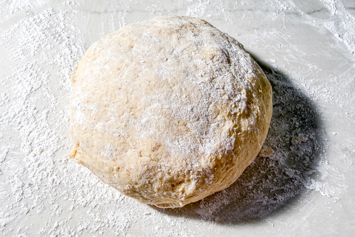 A round ball of raw dough dusted with flour sits on a floured surface, ready for baking or further preparation.