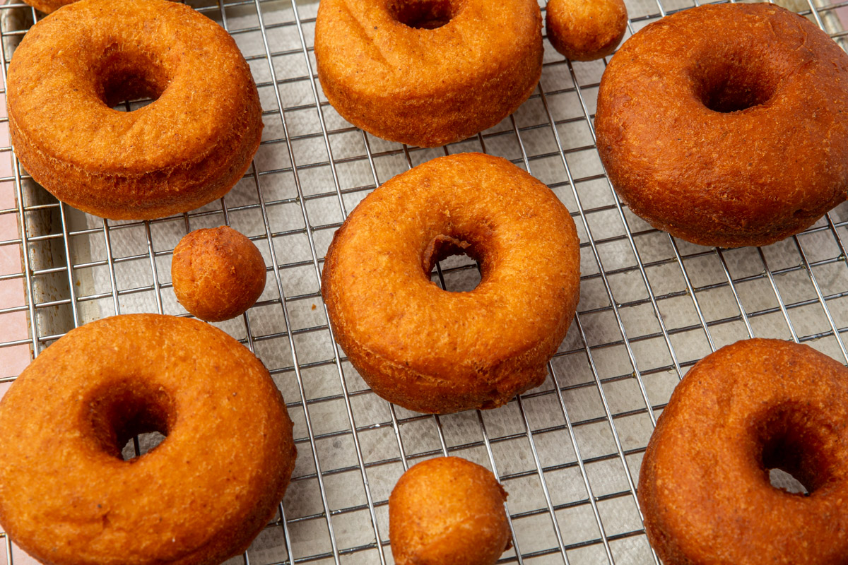 Golden brown cake donuts and donut holes cooling on a wire rack.