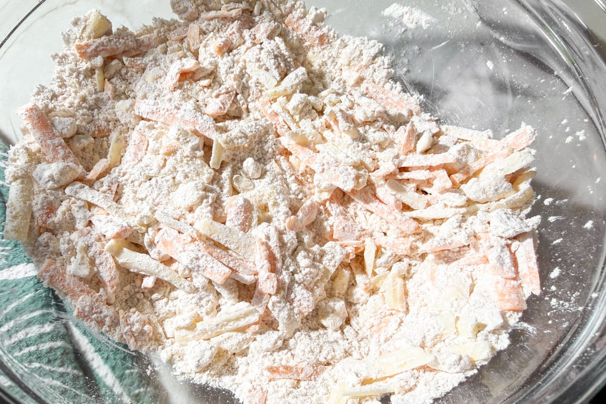 A glass bowl filled with shredded cheddar cheese tossed in a gluten-free flour mixture to make cheddar bay biscuit dough.