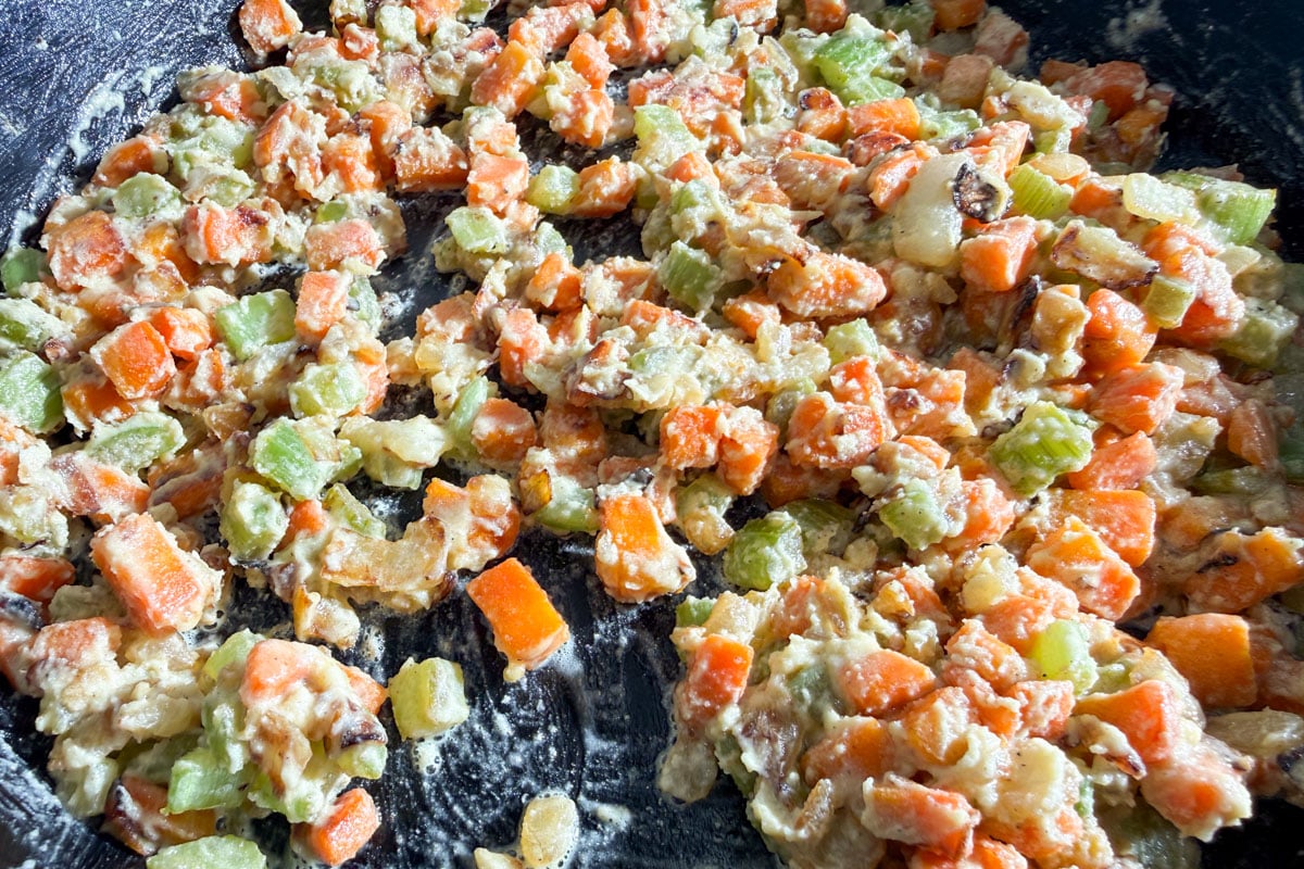 Chopped carrots, celery, and onions being sautéed in a pan with a gluten-free roux, creating a colorful and textured mixture.