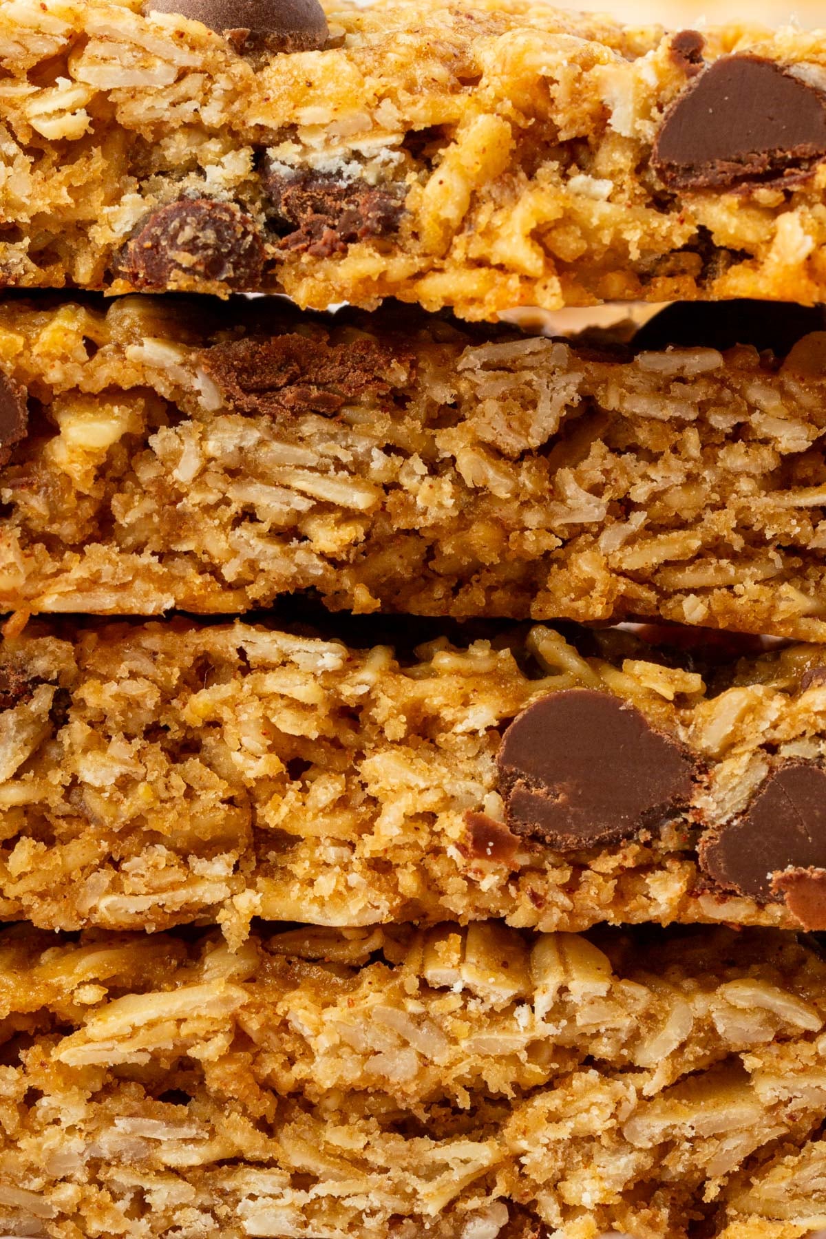 Close-up of four stacked gluten-free oat and chocolate chip granola bars, showing their crumbly texture and layers with melted chocolate chips embedded throughout.