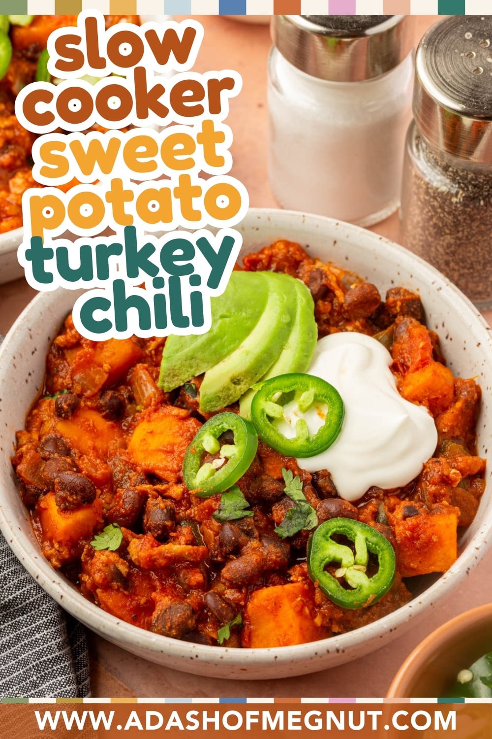 A bowl of turkey chili with sweet potatoes, topped with sliced avocado, jalapeños, and a dollop of sour cream. Slow Cooker Sweet Potato Turkey Chili text overlays the image. Website URL: www.adashofmegnut.com.