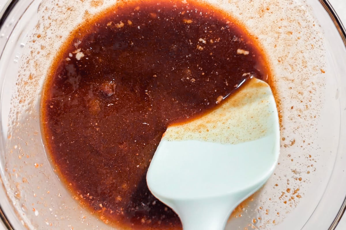 A spatula stirring a melted butter and cinnamon mixture in a clear glass bowl.