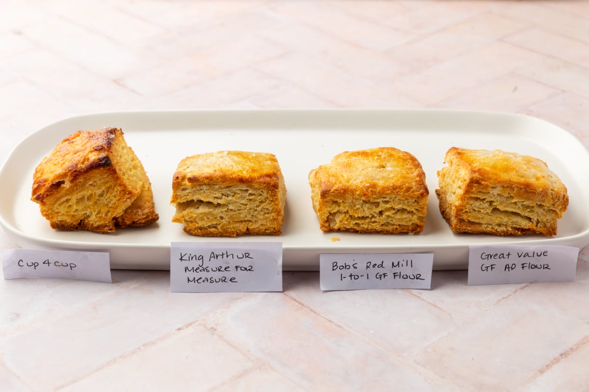 Four square biscuits are lined up on a white tray, each labeled with a different gluten-free flour brand: Cup 4 Cup, King Arthur Measure for Measure, Bob’s Red Mill 1-to-1 GF Flour, and Great Value GF AP Flour.