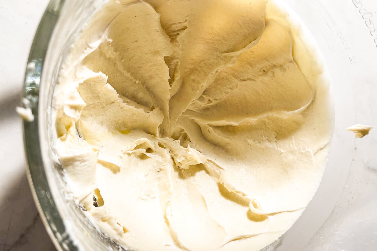 Close-up of smooth, creamy gluten-free focaccia dough in a glass mixing bowl with visible swirls and ridges from mixing.