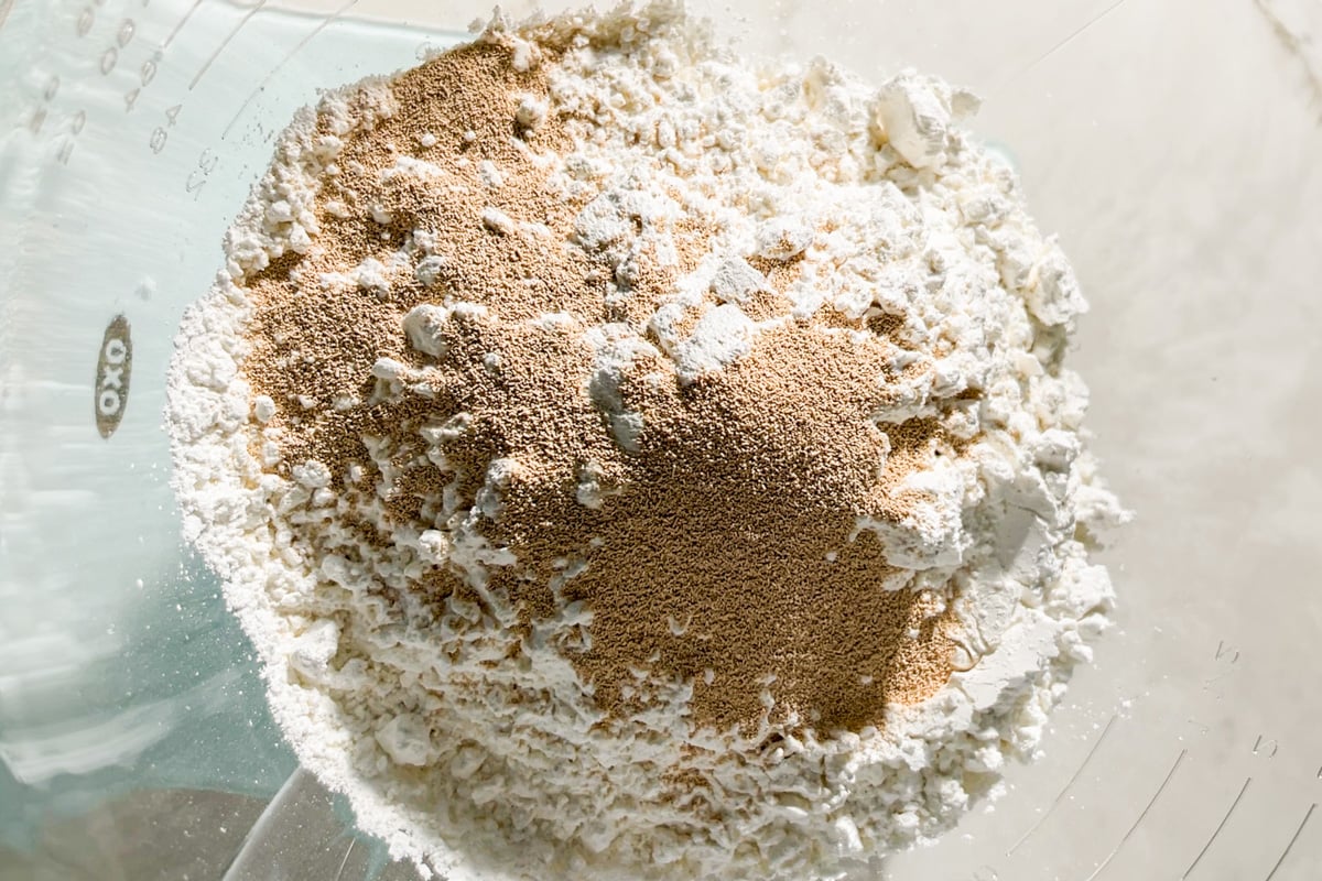 A close-up of a glass mixing bowl containing Caputo Fioreglut flour, instant dry yeast, salt and sugar, ready to be mixed for baking focaccia.