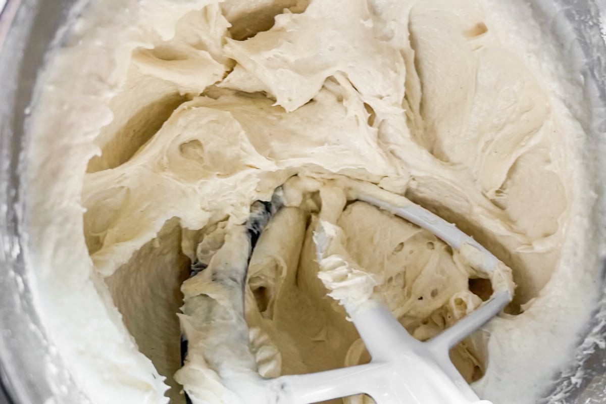 Close-up of thick, creamy gluten-free focaccia dough being mixed in a stand mixer with a white paddle attachment. The batter clings to the sides of the bowl and the paddle.