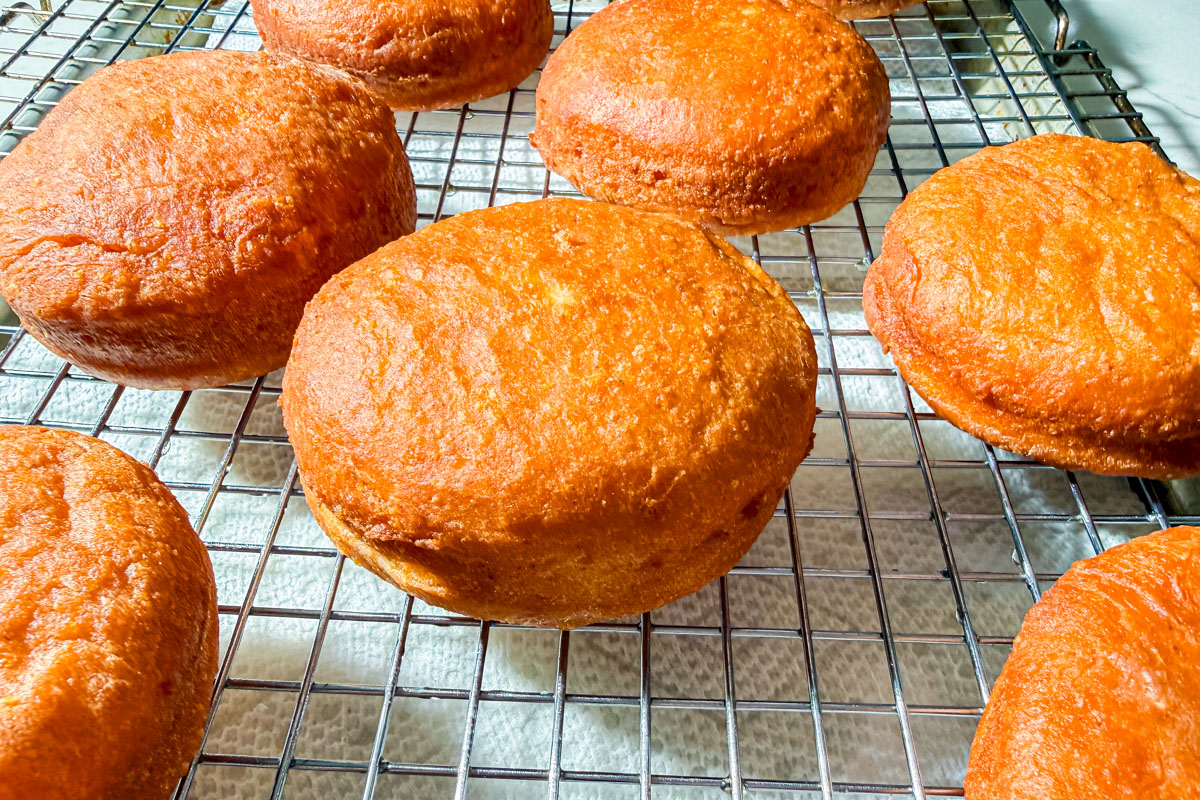 Golden brown, round pieces of fried dough rest on a cooling rack, with sunlight highlighting their crispy texture.