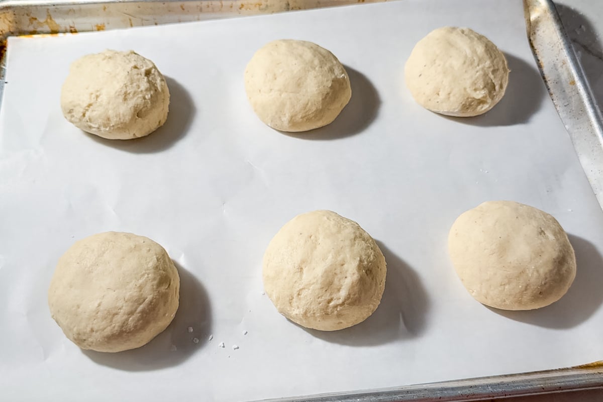 Six unbaked dough balls are evenly spaced on a parchment-lined baking sheet, ready to be baked.