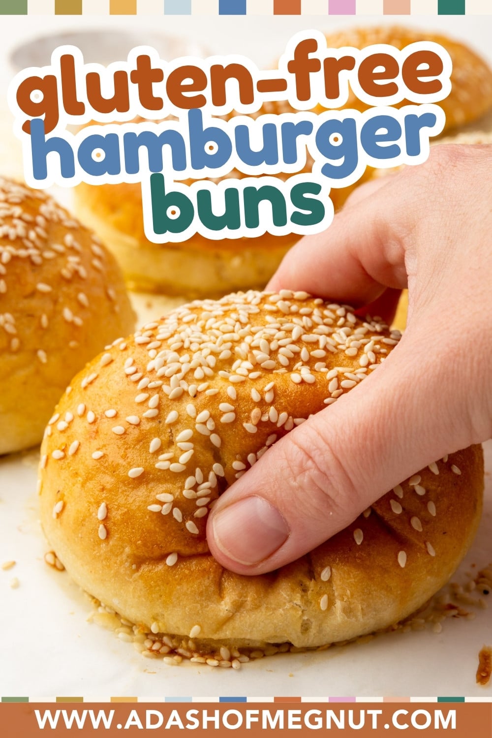 A hand picking up a sesame seed-topped gluten-free hamburger bun, with more buns in the background and colorful text above reading “gluten-free hamburger buns.” Website URL appears at the bottom.