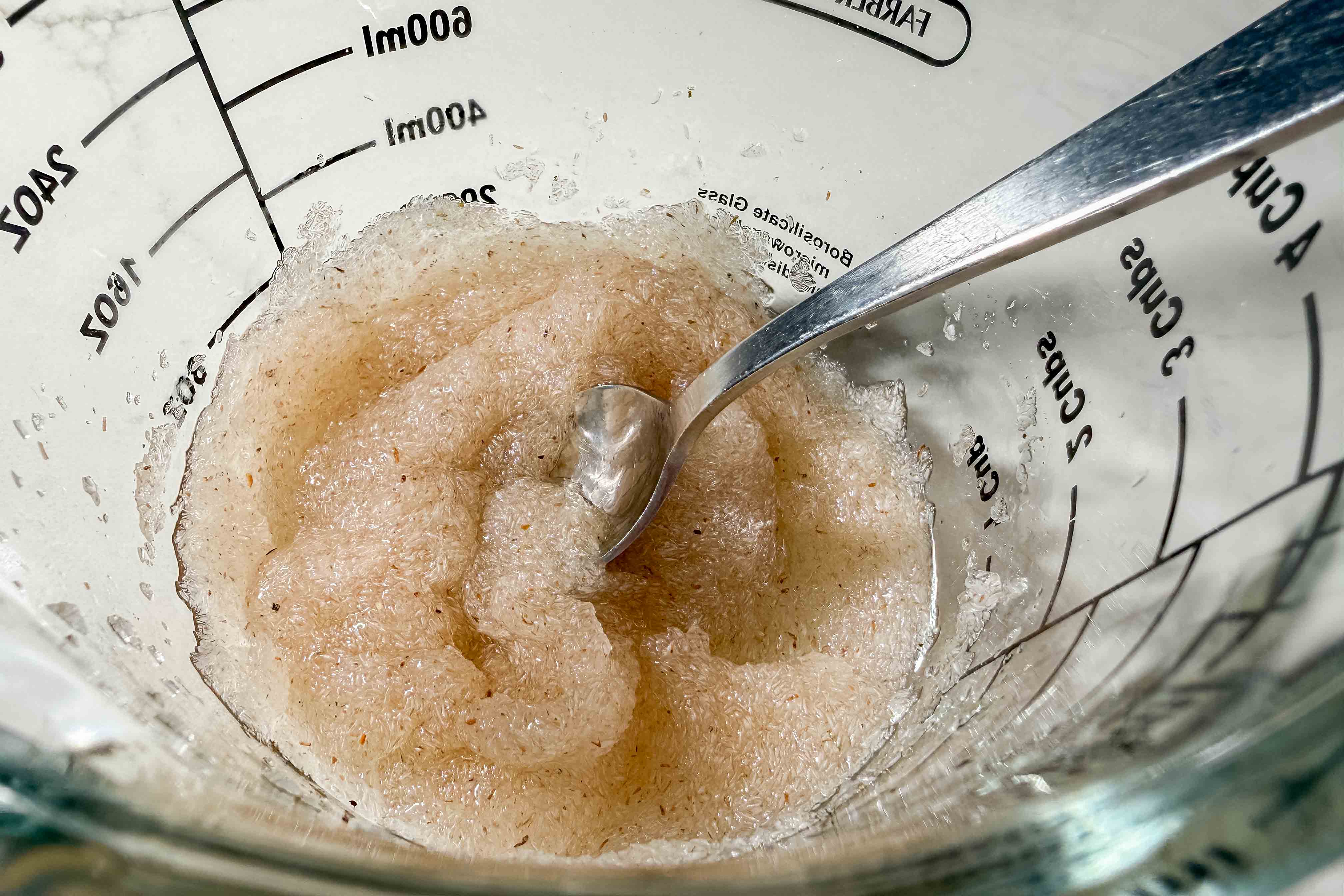 A close-up of a thick, psyllium gel mixture in a glass measuring cup with a metal spoon.