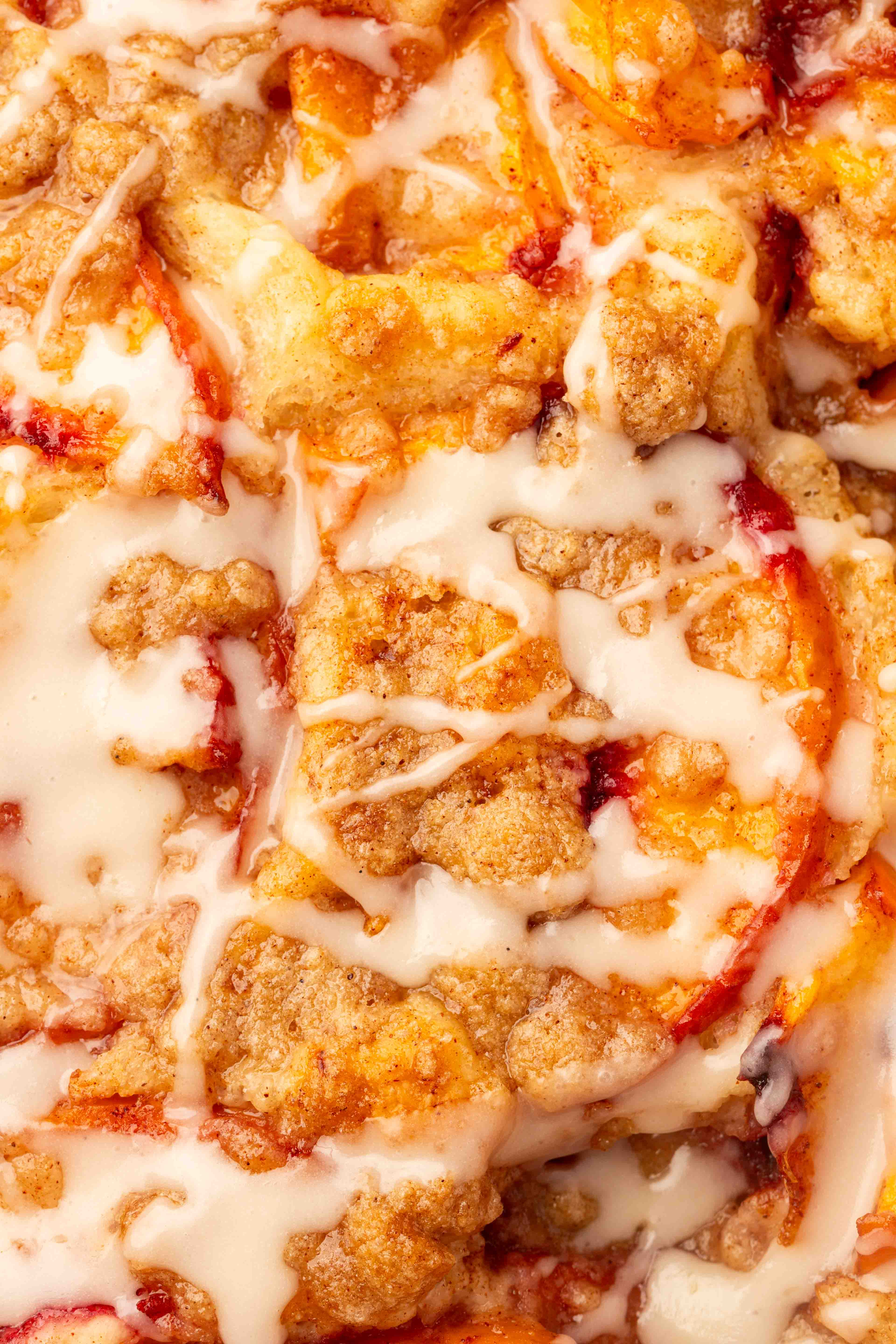 Close-up of a Gluten-Free Peach Crumble Focaccia topped with crumbly streusel and drizzled with white icing, showing golden-brown baked crust and slices of peaches.