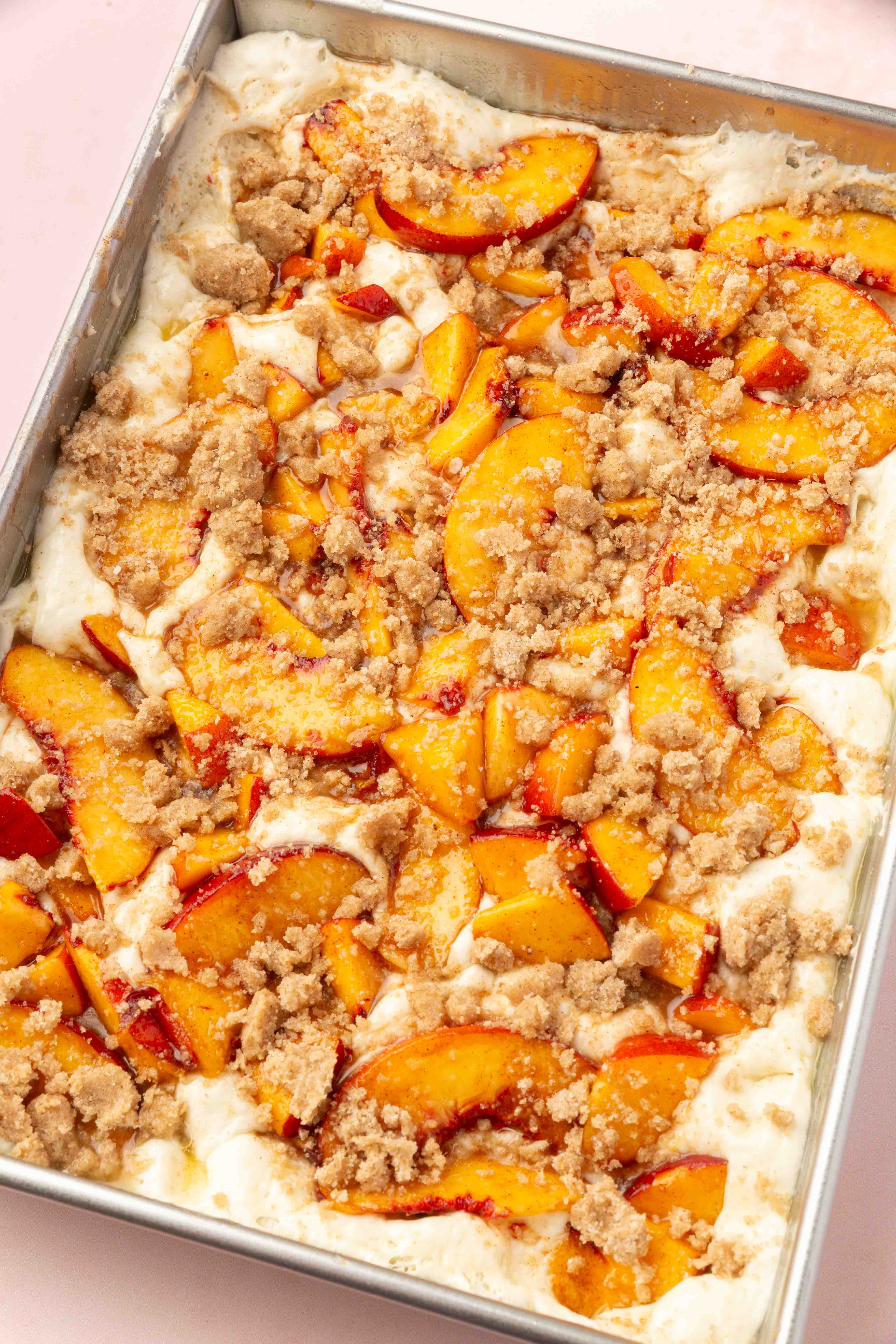 Sliced peaches and crumbly streusel topping on a creamy batter in a rectangular baking pan, ready to be baked into a delicious Gluten-Free Peach Crumble Focaccia.