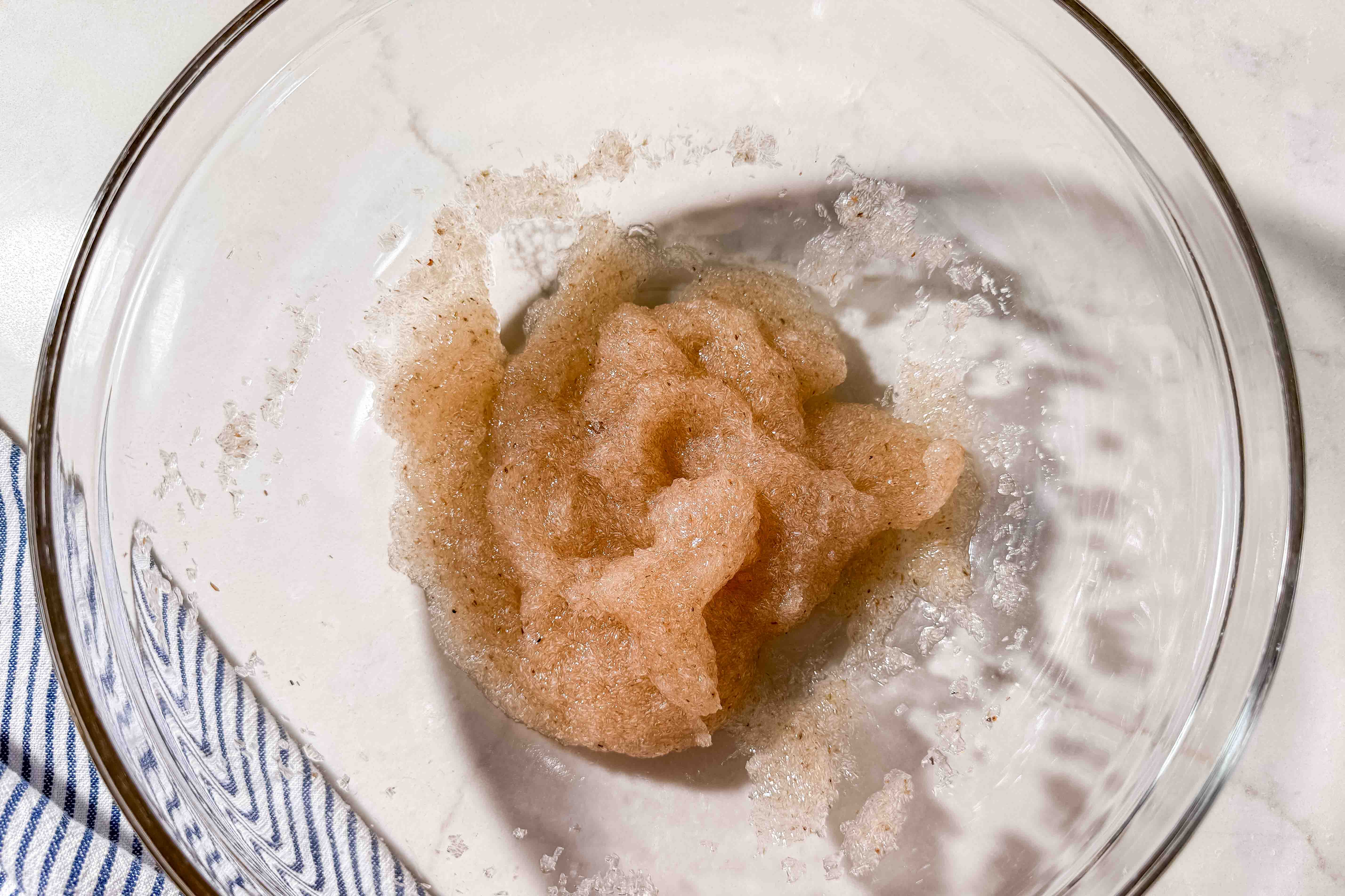 A glass bowl containing psyllium husk gel. A striped cloth is partially visible underneath the bowl.