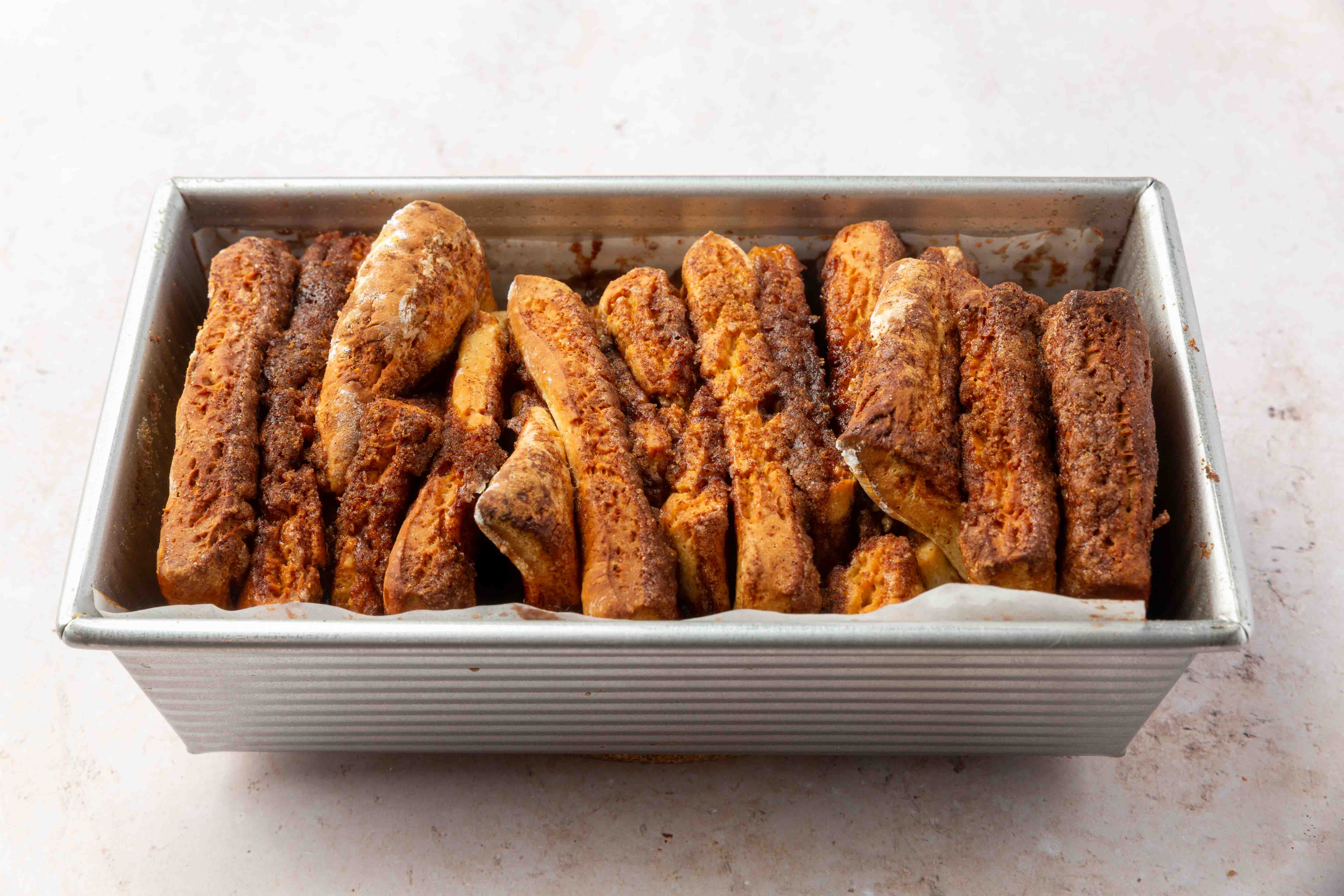 A metal loaf pan filled with slices of cinnamon pull-apart bread, with a golden-brown crust and visible cinnamon sugar on top.
