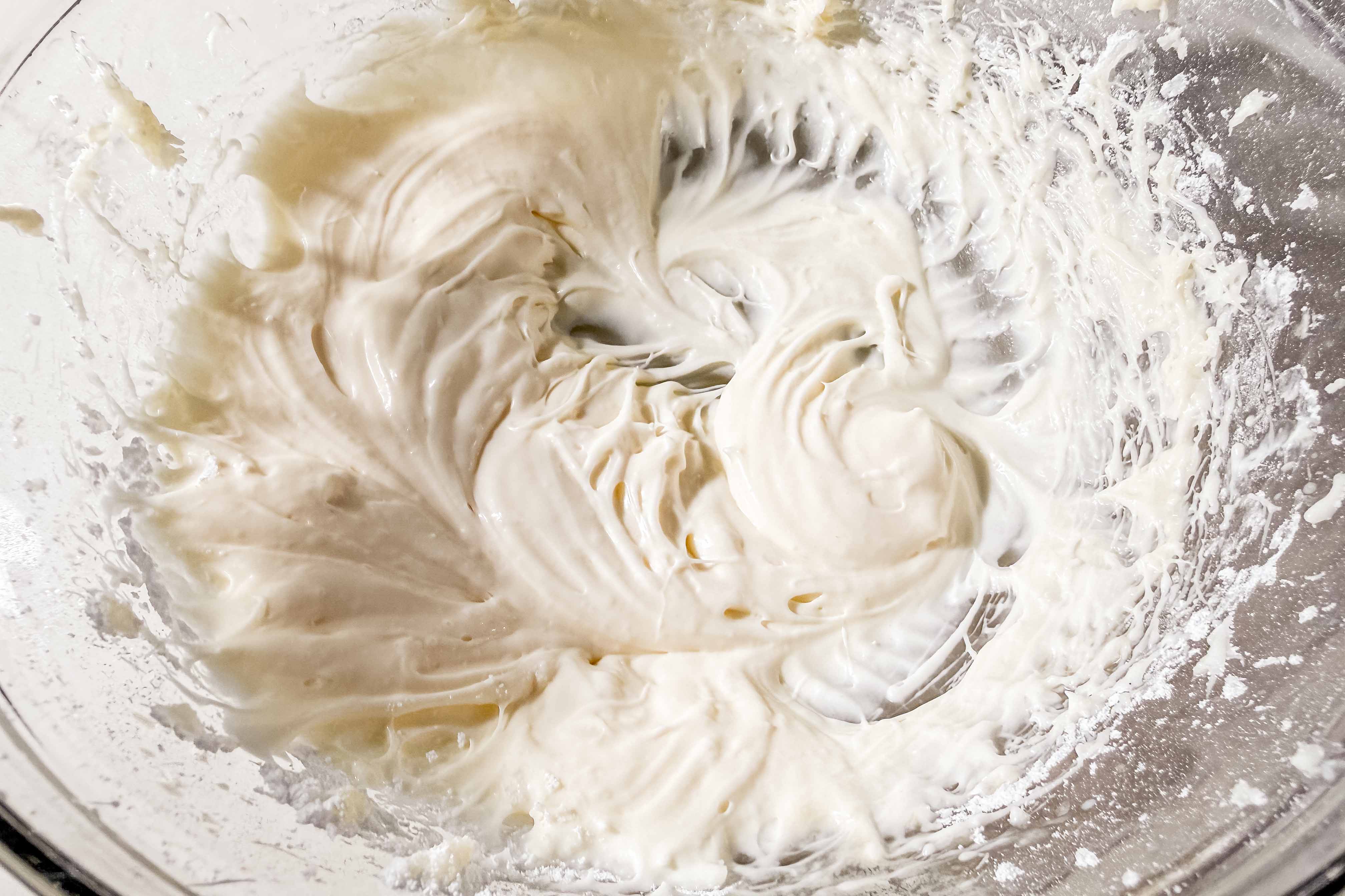 A glass bowl with creamy, whipped white cream cheese icing swirled in the center with peaks and ridges along the sides.