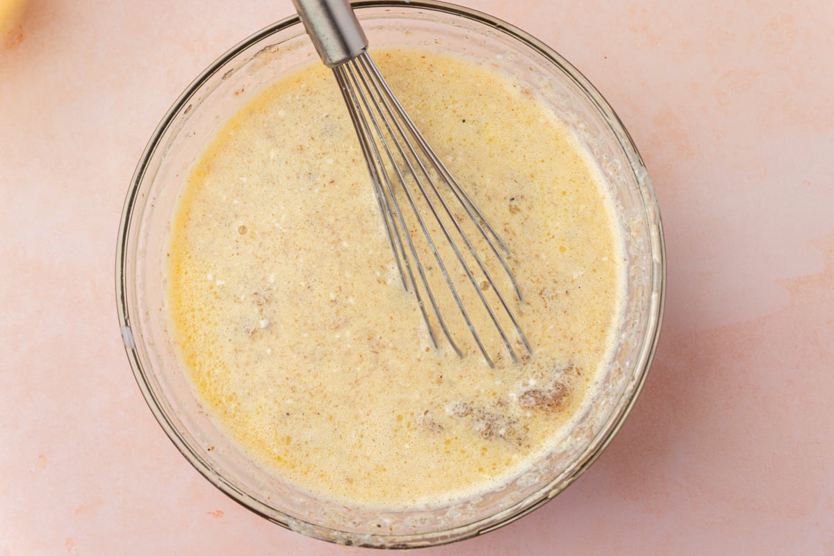 A glass bowl filled with wet ingredient for gluten-free pull apart cinnamon bread, including melted butter, egg, milk, and psyllium husk.