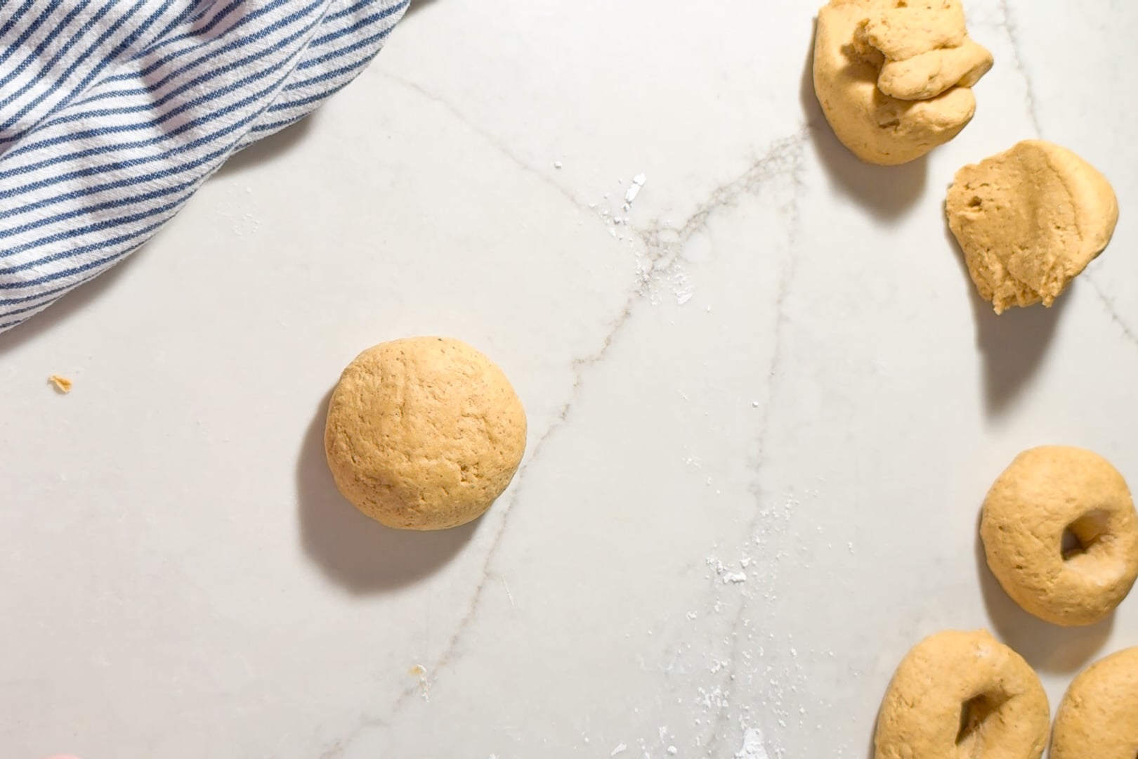 Several balls of raw gluten-free pumpkin bagel dough on a white countertop next to a blue and white striped towel.