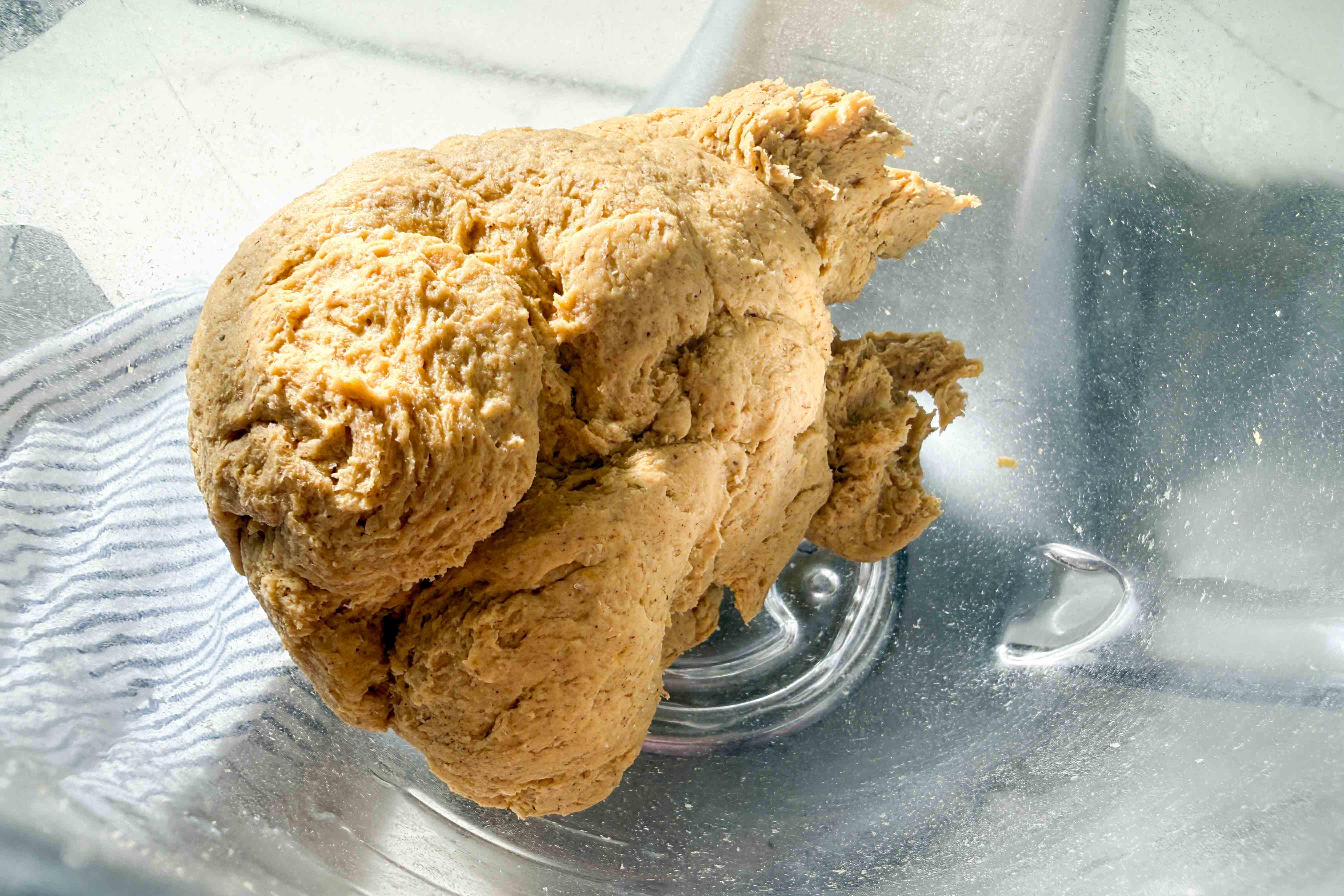 A ball of pumpkin bagel dough in a clear glass mixing bowl.