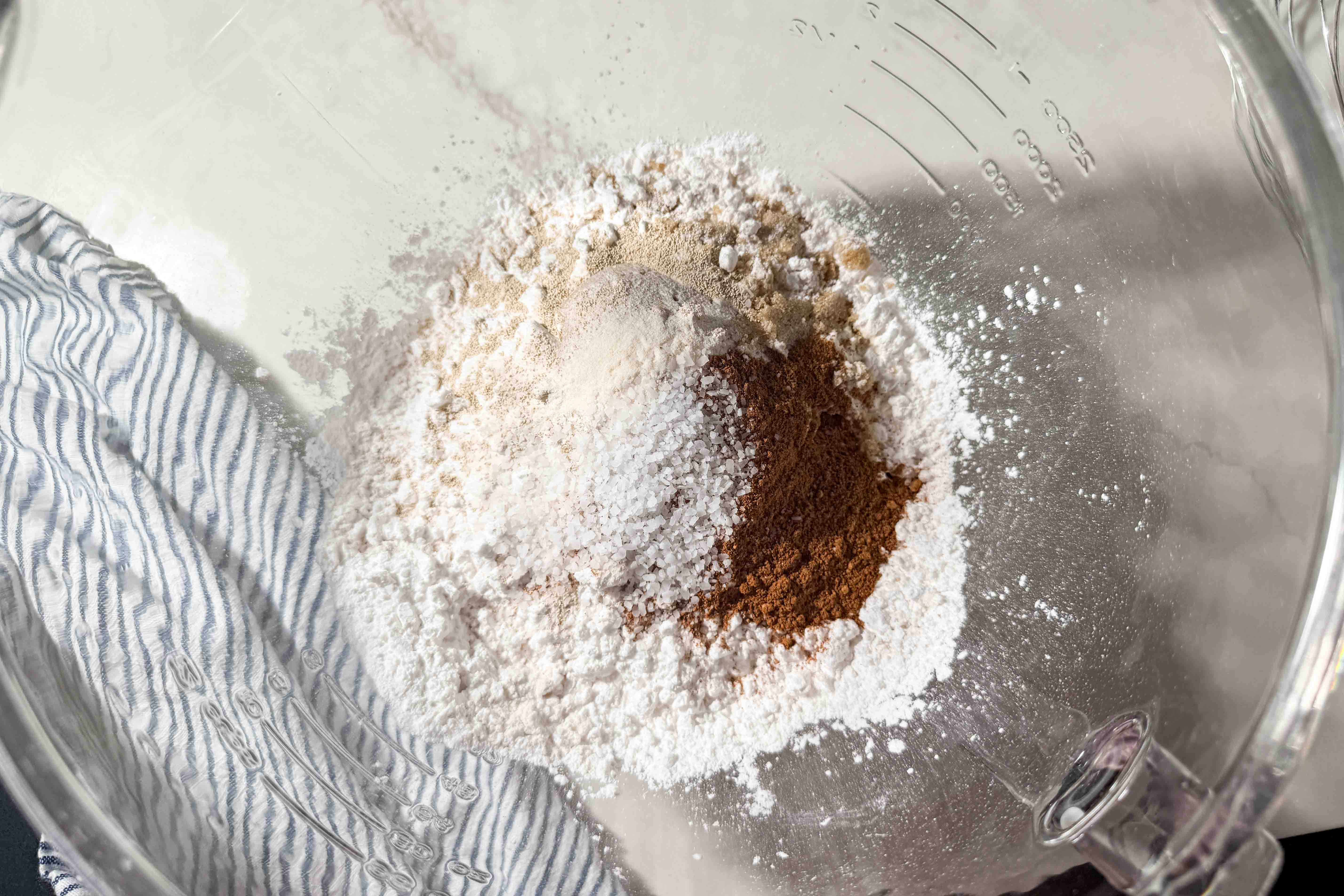 A glass mixing bowl with gluten-free flour, salt, yeast, pumpkin pie spice, and xanthan gum.