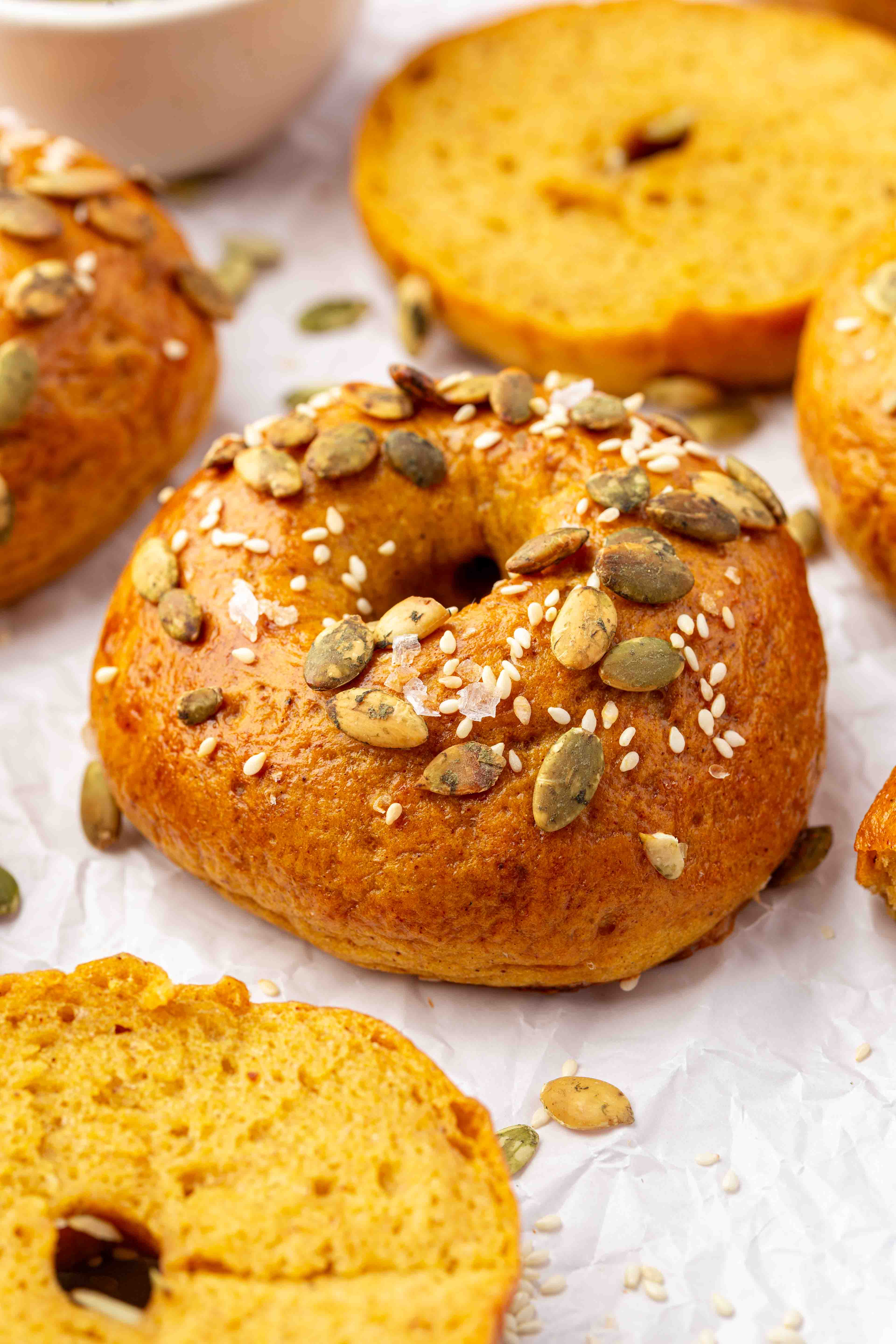 Golden pumpkin bagels topped with pumpkin seeds, sesame seeds, and sea salt on parchment paper.