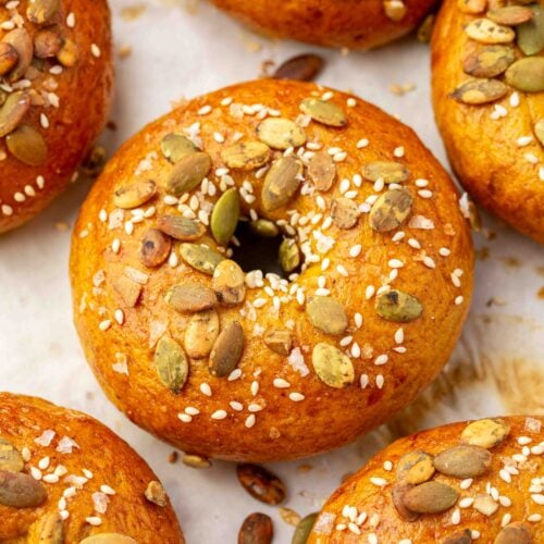 Several golden-brown gluten-free pumpkin bagels topped with pumpkin seeds, sesame seeds, and coarse salt.
