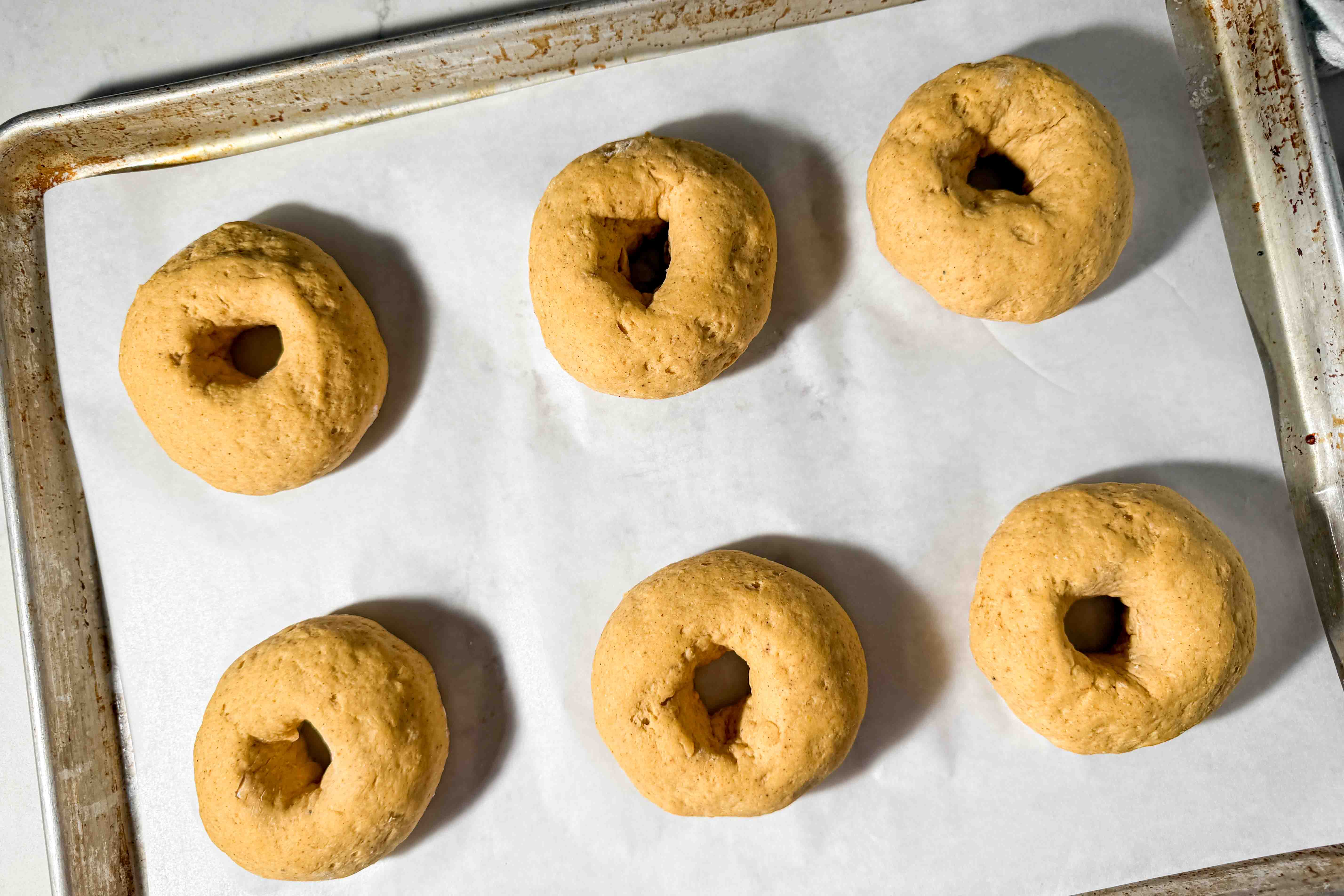Six puffy pumpkin bagel dough rounds arranged on a parchment-lined baking sheet after proofing.