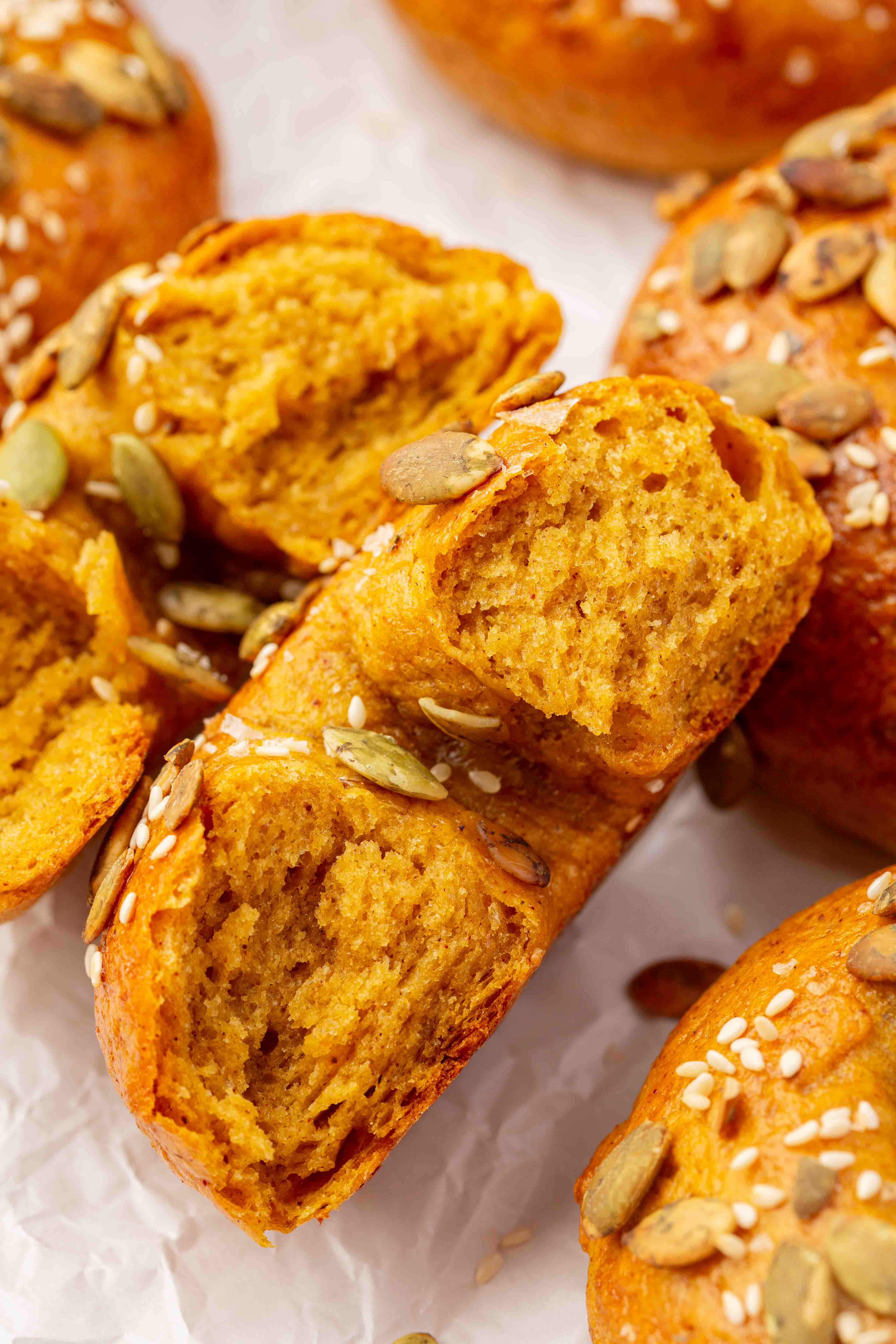 Golden-brown pumpkin bagels topped with pumpkin seeds and sesame seeds, one pulled apart to reveal the soft, orange interior.