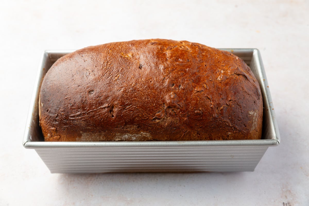 A loaf of dark brown baked gluten-free bread in a rectangular metal loaf pan.