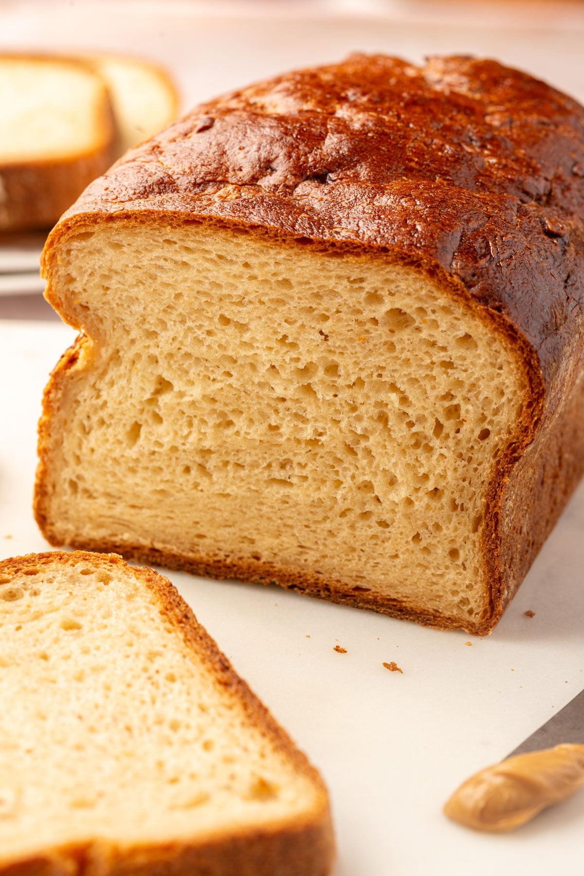 A sliced loaf of gluten-free bread on a cutting board next to a single slice and a small dollop of peanut butter.