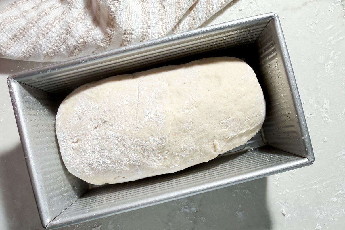 A rectangular loaf of raw gluten-free bread dough in a metal loaf pan.