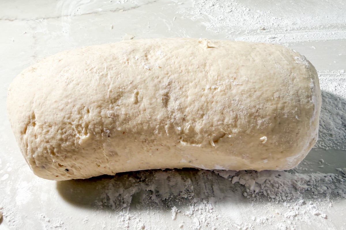 A shaped log of raw gluten-free sandwich dough resting on a floured surface.