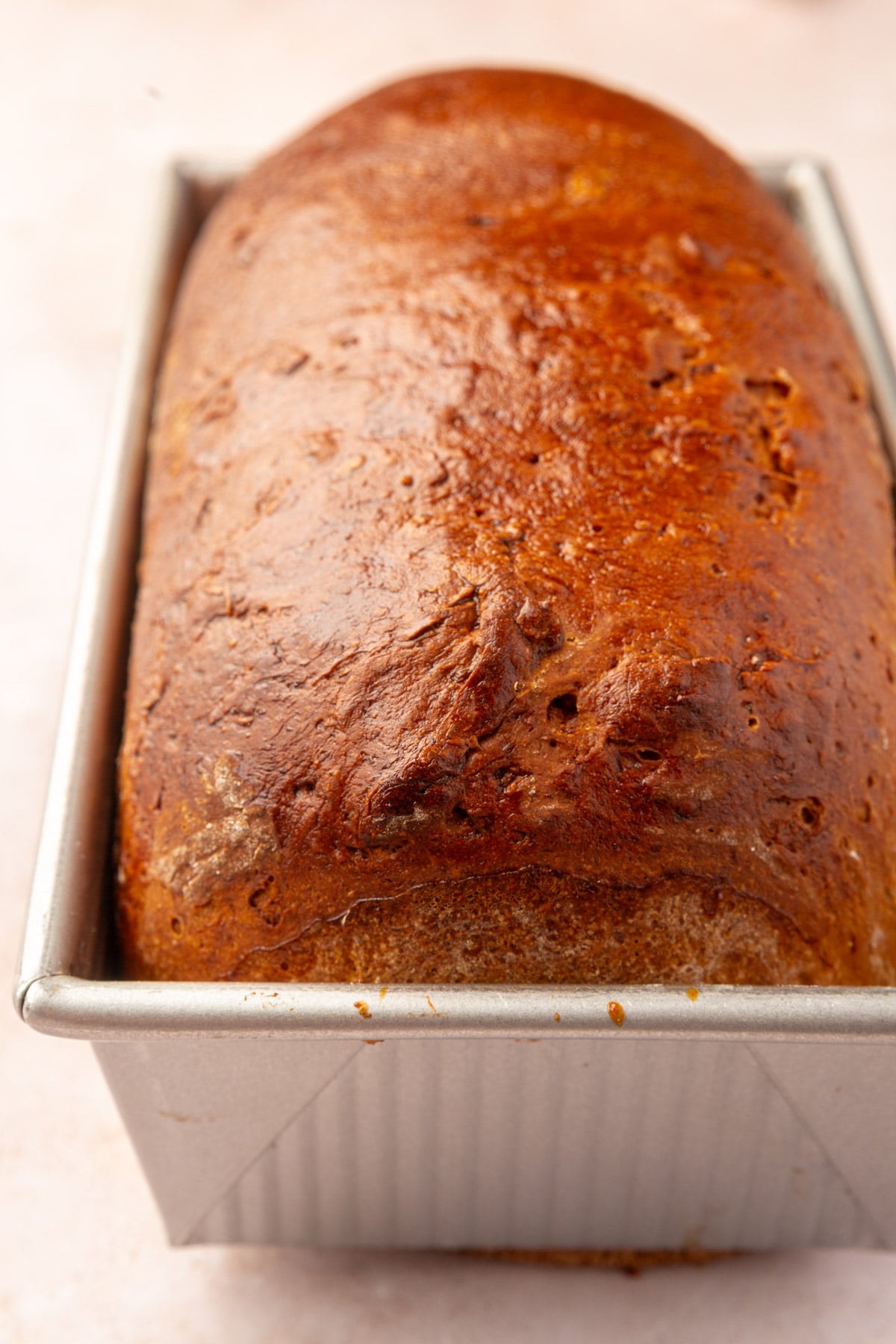 A loaf of golden-brown baked gluten-free sandwich bread in a rectangular metal loaf pan.
