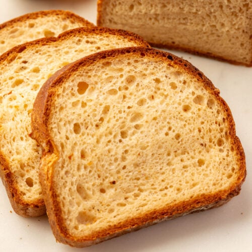 Three slices of gluten-free bread and a partial loaf on a marble surface, with a small bowl of spread in the background.