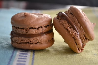 Two chocolate maracarons with nutella filling leaning on each other.