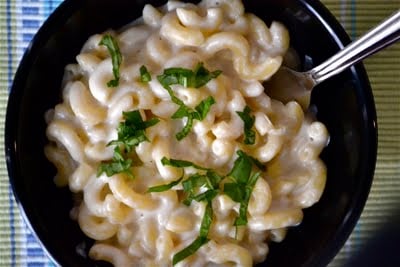 A bowl of mozzarella mac and cheese topped with basil and a spoon.