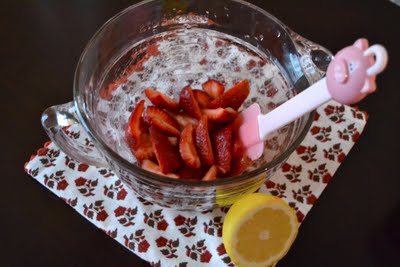 A bowl of sugar and strawberries with a lemon on the side.