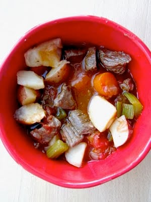 A bowl of beef stew with carrots and celery in a red bowl. 