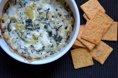 A bowl of hot spinach artichoke dip with crackers on the side.