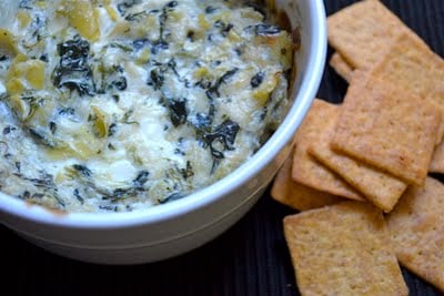 A bowl of spinach artichoke dip with crackers on the side.