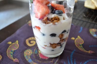 A glass with yogurt, peanut butter granola, strawberries and blueberries. 