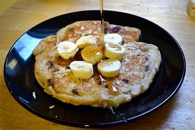 A chocolate chip pancake topped with sliced bananas and maple syrup. 